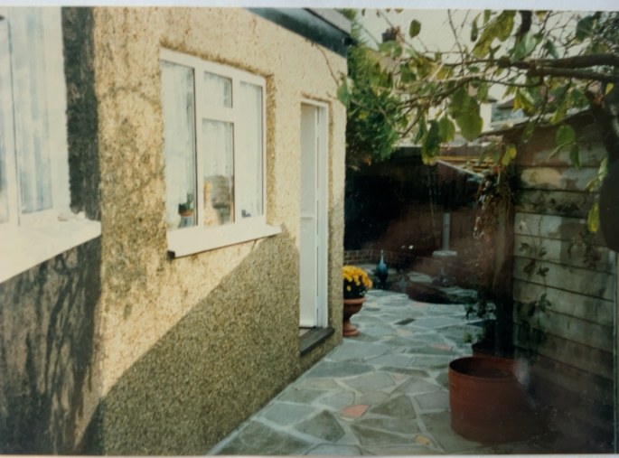 Original archive photograph: completed pebbledashed extension in West Croydon, Surrey, with a white window and door opening onto a crazy-paved patio with planted pots