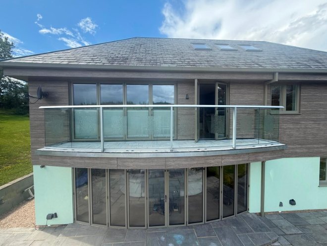 Completed curved glass balcony with tiled deck on a detached house