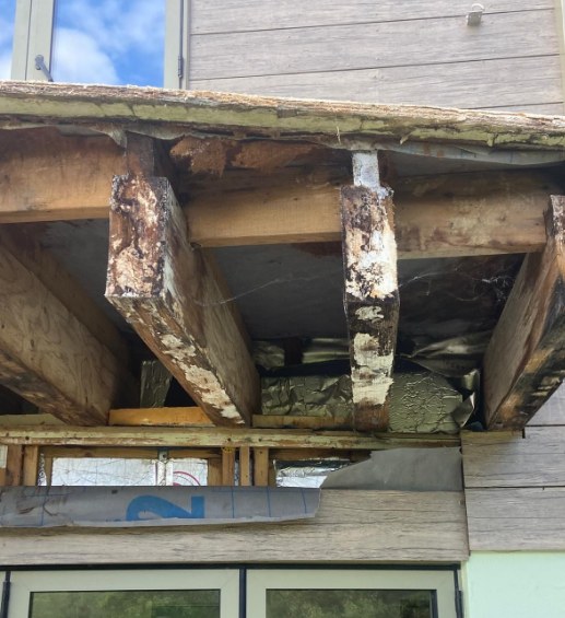 Rotted and flaking balcony joists exposed beneath the old deck